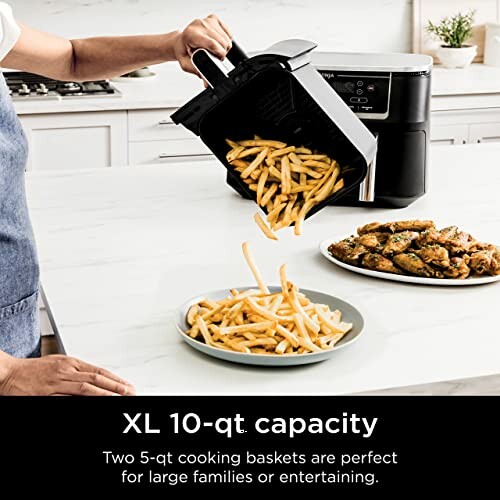 Person serving fries from dual air fryer onto plates with wings nearby